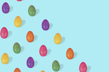 Creative Easter pattern made of colorful eggs arranged on pasel blue background.
