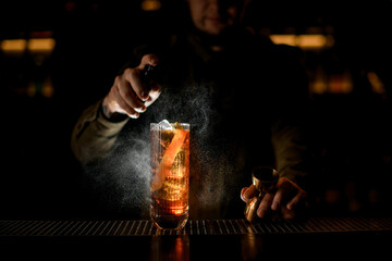 beautiful illuminated glass of drink stands on bar and man bartender sprinkles on it