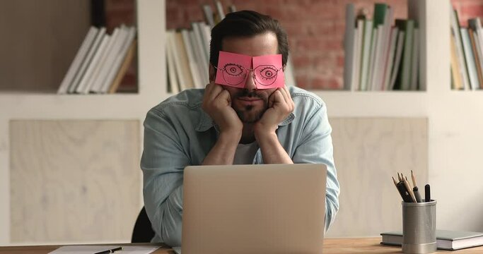 Tired sleepy inefficient indifferent employee with pink adhesive notes on his eyes yawns sleeps sit at workplace, worker feels bored due routine work. Lack of interest, energy, not inspired concept
