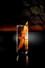 view of illuminated transparent glass with cold drink with zest standing on bar counter