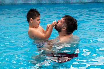 child with disability laughs and plays in his father's arms in a swimming pool