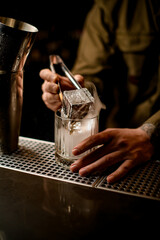 Close-up view of steaming glass in which bartender put piece of ice using tongs