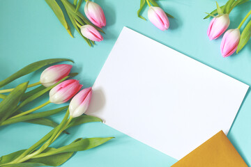 blank white paper page with golden envelope and beautiful pink tulip flowers on blue background