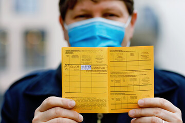 Man with medical mask holding German inernational certificate of the vaccination. He showing the...