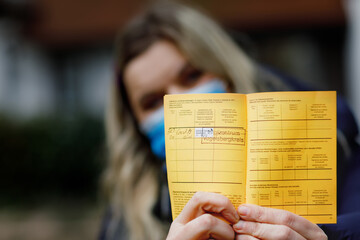 Woman with medical mask holding German inernational certificate of the vaccination. Adult showing...