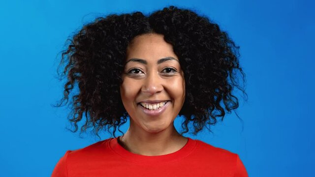 African woman with curly hair looking to camera, smiling. Beautiful model girl on blue studio background.