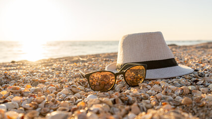 Fototapeta na wymiar Hat, sunglasses on the beach with a shell on a sunset, vacation concept