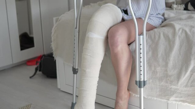 A woman after surgery on her leg in a longitudination and bandages gets out of bed on crutches.
