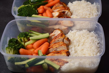 Healthy balanced lunch boxes. Grilled chicken, carrots, cucumbers, broccoli, and white rice. Lunch boxes with food ready to go for work or school. Office food lunch concept