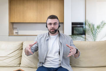 Young man with headset looking at camera and using video chat in home office  