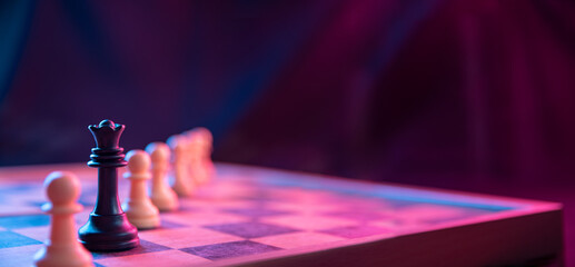 Chess pieces on a chessboard on a dark background shot in neon pink-blue colors. The figure of a...