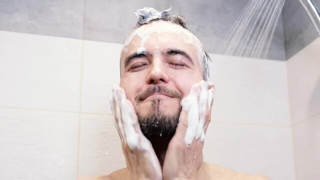Man wellness, body care and personal hygiene concept. Handsome caucasian guy washing hair and beard with shampoo in bathroom, smiling and enjoying showering under water. Morning routine.