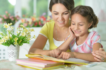 little cute girl reading book with mother at the table at home