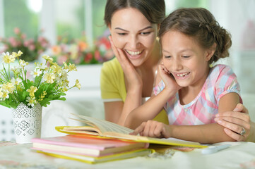 little cute girl reading book with mother at the table at home