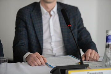 Businessman giving interview at table with microphones, closeup. Journalist conference