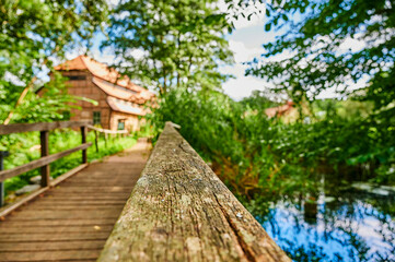 Obraz premium Wooden bridge over a creek as part of an old small weir near a historic watermill. The view goes along the wooden handrail.