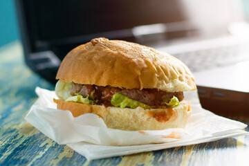 Burger with beef cutlet, sauce and salad in a craft bag for food and laptop side view copy space. Food delivery concept, restaurants operating in quarantine covid 19