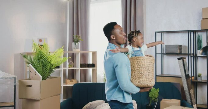 Handsome loving smiling young african american father playing with his small daughter which climbing inside into basket and depicted plane