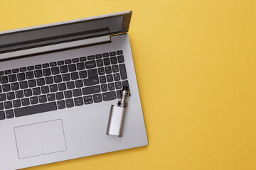 Laptop and vaping device on yellow background. Flat lay