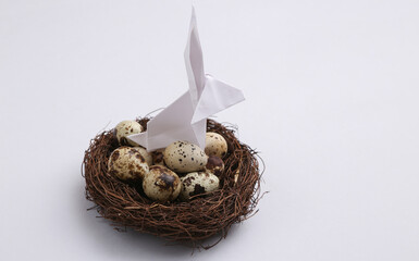Easter composition. Origami Easter bunny and quail eggs in nest on gray background. Top view