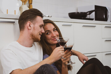 authentic picture of young caucasian couple sitting in the kitchen together and drinking wine for lunch in anniversary day