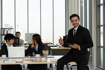 portrait of young caucasian businessman standing in office with background multiethnic colleagues working together. business concept