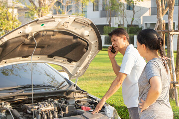 broken car calling for help on cell phone. broken car on the road. asian man and woman near broken car outdoors.
