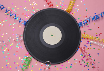 Vinyl record and colored streamer with confetti on a pink background. Music day