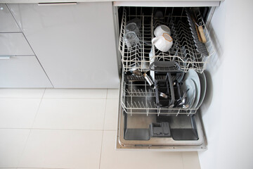 Open dishwasher with clean white dishes in the modern kitchen.