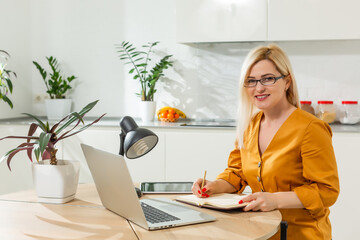 Young woman sitting in kitchen and working on laptop.