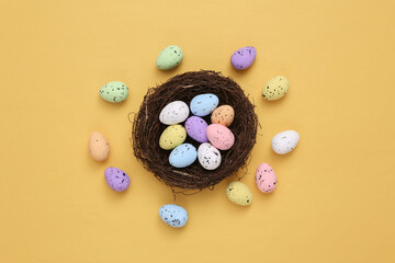 Nest with colored quail eggs on yellow background. Easter composition. Top view