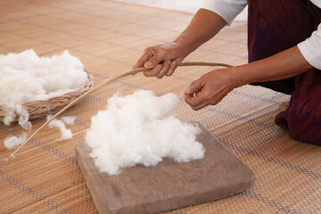 Handmade cotton wool. Closeup of hand using bamboo equipment to make cotton wool fluffy.
Process of making natural cotton wool to fabric. Thai and asian culture. Selective focus