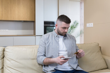 Online shopping concept. Young man holding credit card and using phone at home office Business from home.