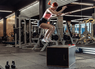 Fit woman in sportswear jump on wooden box in the gym. Intensive functional training