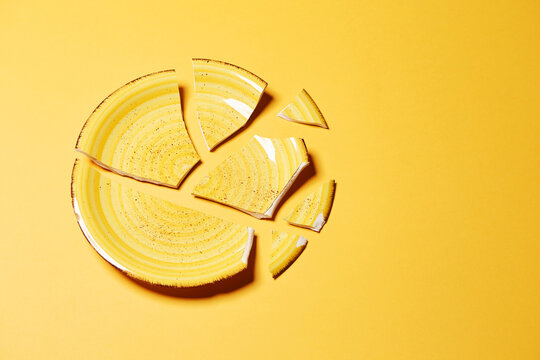 Broken ceramic stylish yellow plate crash with separate large pieces top view isolated on the bright solid yellow fond background