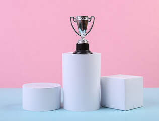 Pedestal of geometric shapes and winner cup on blue pink pastel background