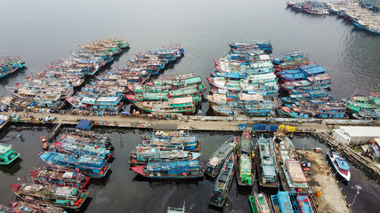 Aerial drone view of Muara Angke Beach with wooden boats leaning beside the pier. With noise cloud after rain. Jakarta, Indonesia. March 21, 2021