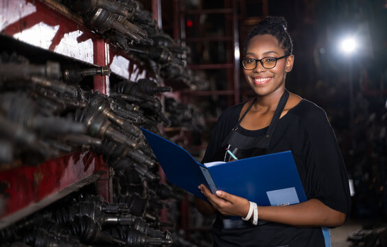 A black woman, business owner or employee in a factory engine parts. Holding the file to check the product list. Smiling and looking at the camera n Business onwner and worker concept.
