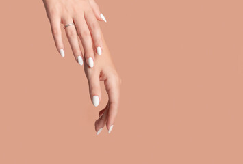 Hands of a beautiful well-groomed woman with feminine nails on a beige background. Manicure, pedicure beauty salon concept. Empty space for text or logo. On nails white gel polish