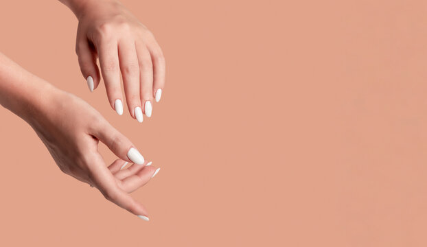 Hands of a beautiful well-groomed woman with feminine nails on a beige background. Manicure, pedicure beauty salon concept. Empty space for text or logo. On nails white gel polish
