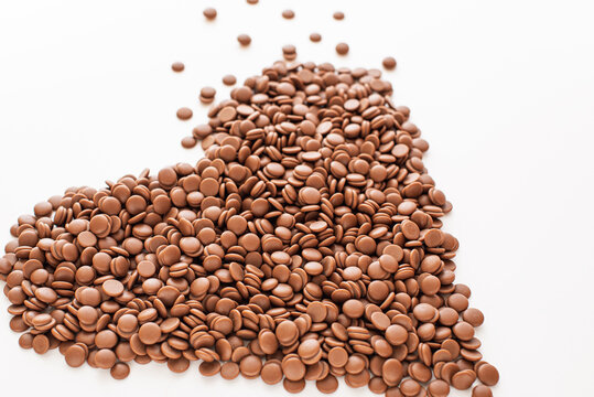 Chocolate callets in bulk on a white background in the form of a heart. The concept of tempered chocolate confectionery. Cooking chocolates by homemade confectioners. Business idea.