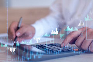 A trader computing historic data to predict stock market behavior. Internet trading concept. Forex and financial hologram chart over the desk and calculator.