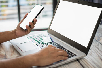 Men holding smartphones with white screen, blank. Businessmen transfer money via internet with smartphones to shop online,  payment. Laptops white screen on desk. Selective focus. Blurred background