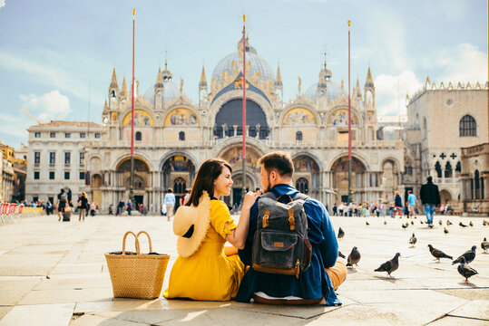 Couple Sitting On The Ground Enjoying The View Of Saint Marco Square Venice Italy