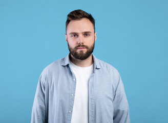 Fototapeta premium Portrait of serious young guy looking at camera on blue studio background