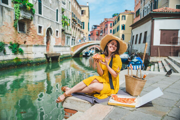woman sitting on pond with view of venice canal eating pizza © phpetrunina14