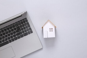 Mini paper house figurine and laptop on gray background. Flat lay
