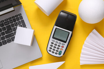 Laptop with pos terminal and geometric shapes on a yellow background. Top view