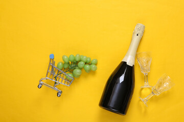 Bottle of wine and grapes in shopping trolley, glasses on a yellow background