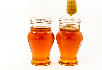Honey dripping from wooden stick into glass jar, whte background